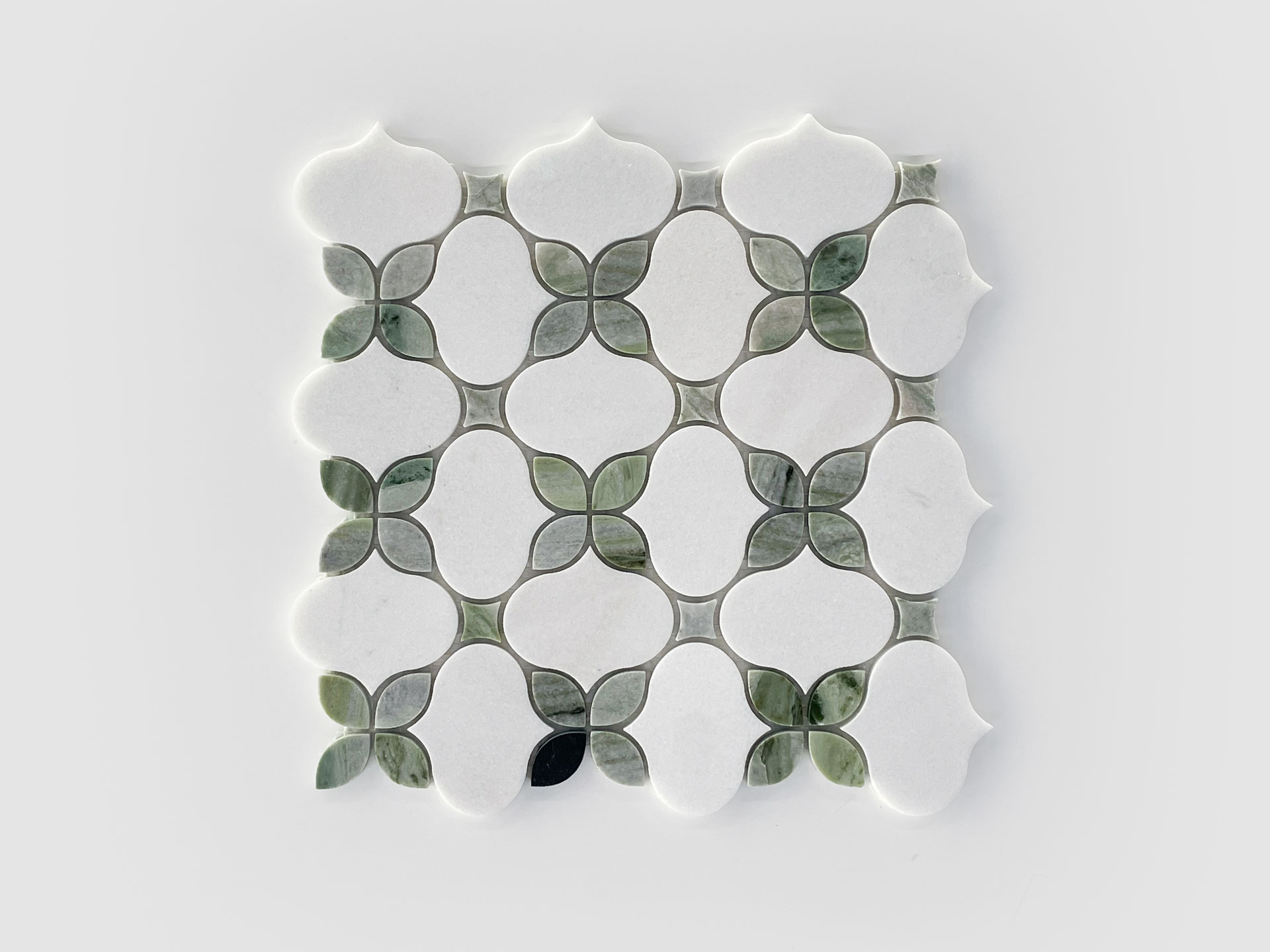 A square tile sheet featuring a geometric pattern of white shapes bordered by smaller, green leaf-like tiles on a light gray background. The design creates a repeating, symmetrical motif.