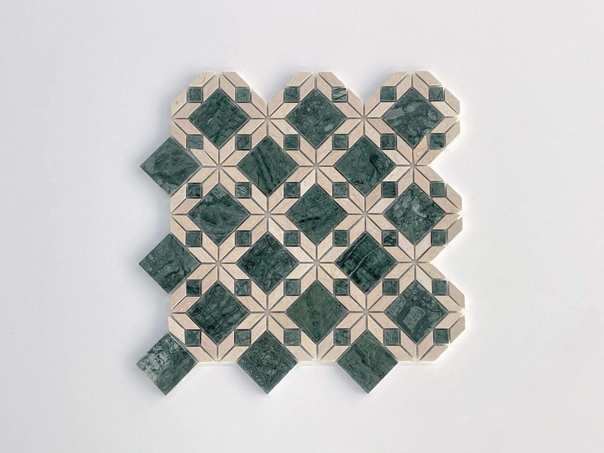 A decorative tile mosaic featuring a geometric pattern with green and beige shapes arranged in a symmetrical, repeating design on a white background.