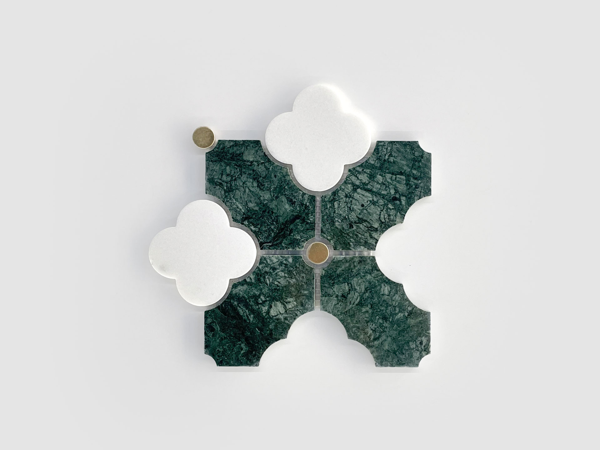 A geometric design with four green marble tiles featuring white, quatrefoil-shaped tops, arranged in a square. Three small gold circular accents are placed at some intersections on a plain gray background.