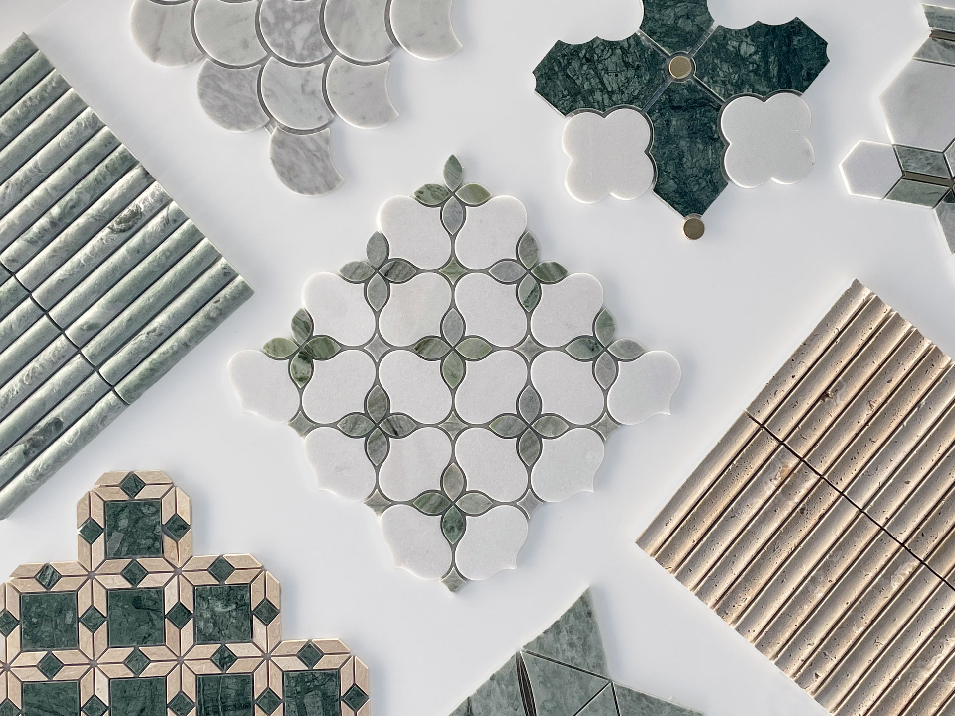 An assortment of decorative ceramic and marble tiles in various shapes, patterns, and shades of green, white, and beige, arranged neatly on a white surface.