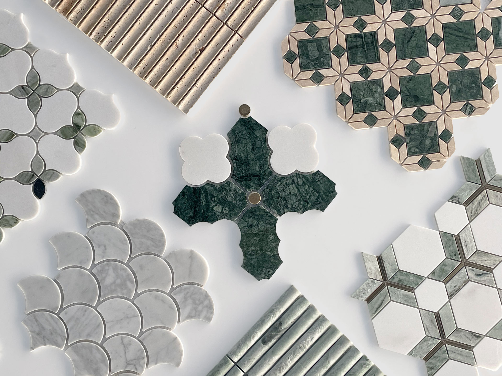 A collection of decorative tiles in various shapes, patterns, and colors, including green, white, and beige, arranged on a white surface. Some tiles are geometric while others have curved or scalloped designs.