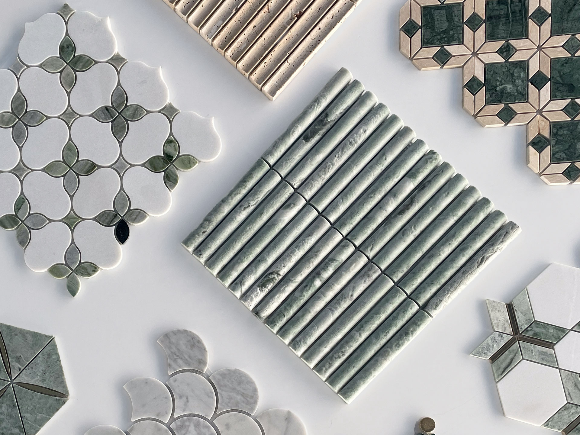 A selection of decorative tiles in various geometric patterns and colors, including green, white, and beige, displayed on a light surface. The tiles feature shapes like hexagons, circles, and lines.