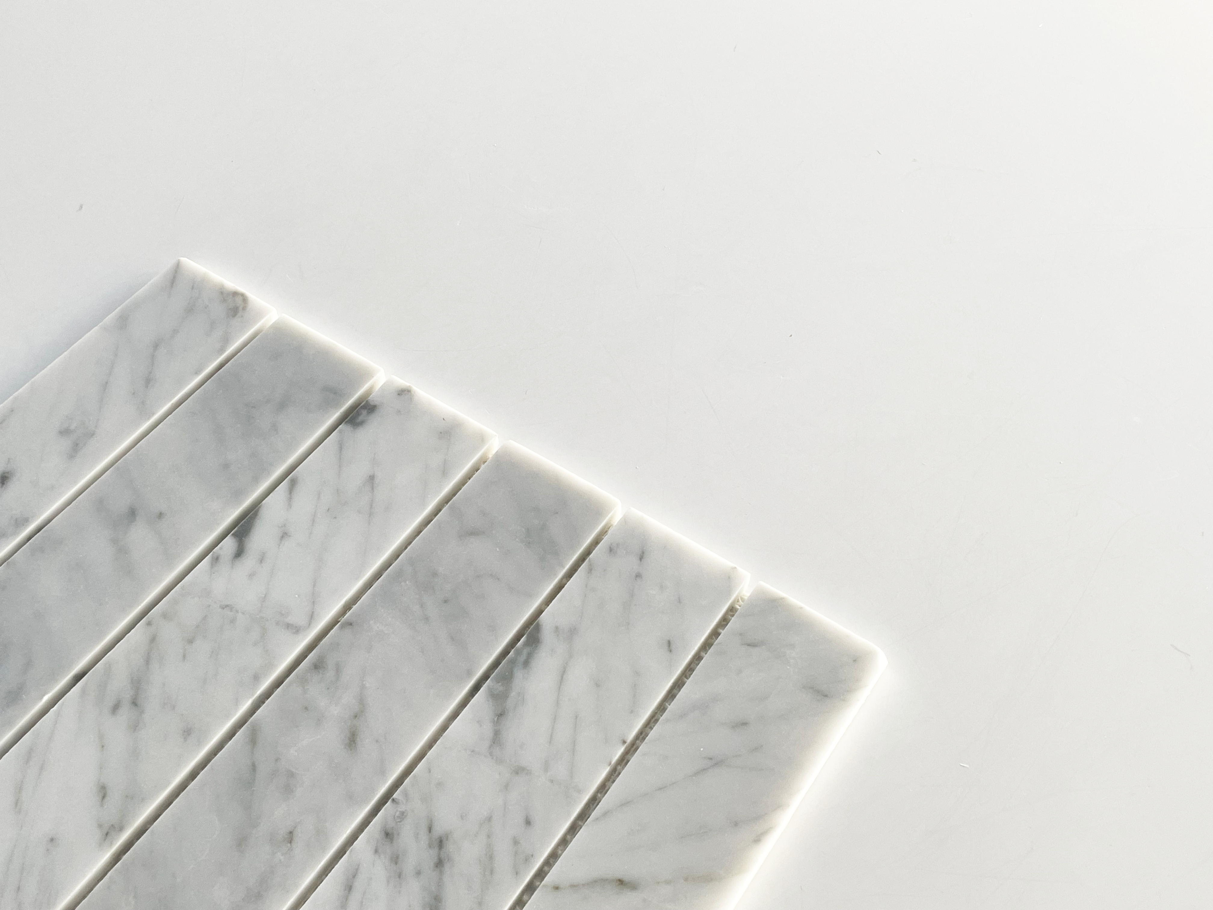Seven rectangular strips of white marble with gray veining are arranged in parallel on a white surface, occupying the lower left corner of the image with ample negative space around them.