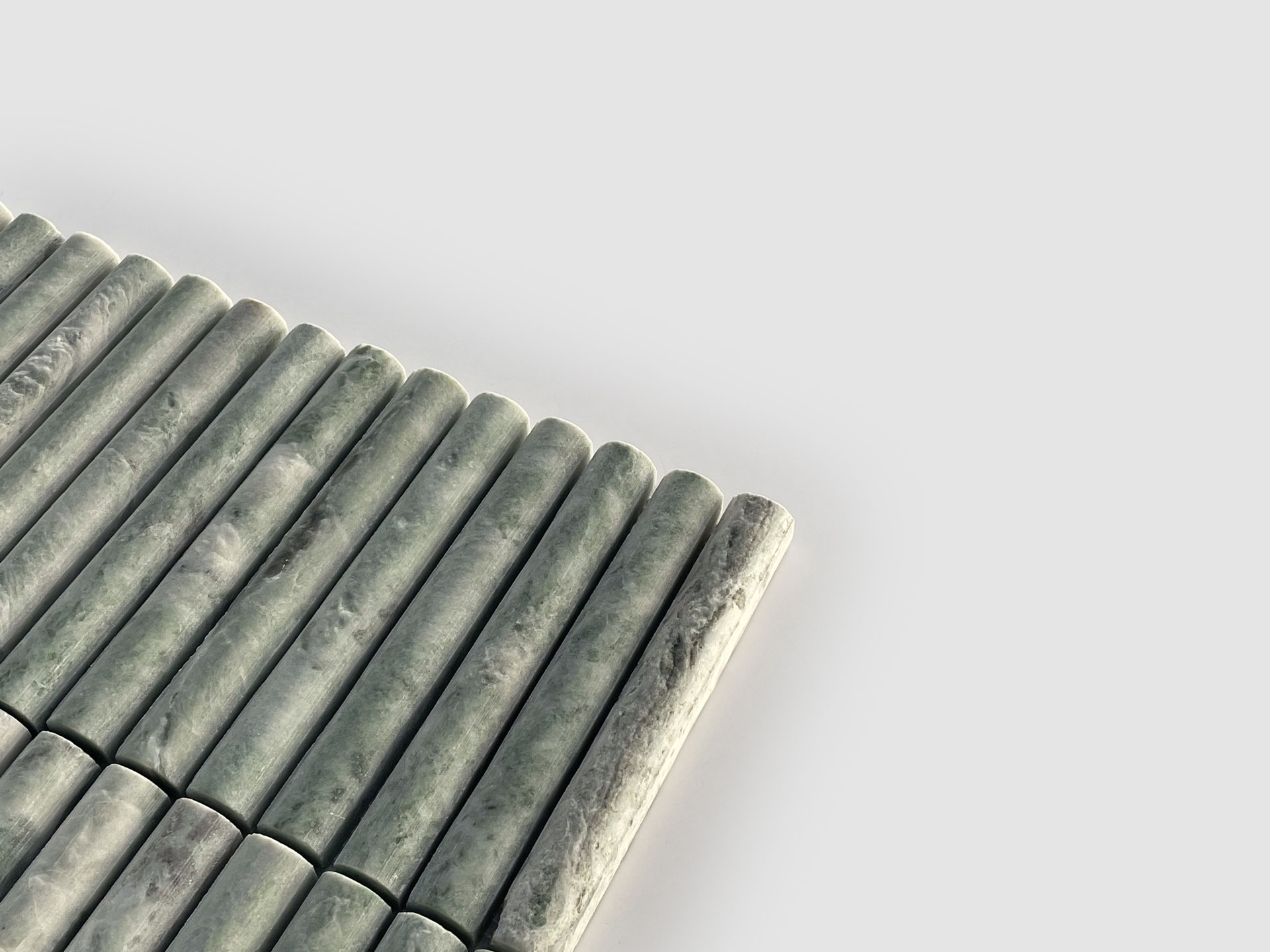 A close-up of evenly spaced, cylindrical green marble rods arranged in parallel rows on a light gray background. The rods have a smooth, polished surface with natural marbling patterns.