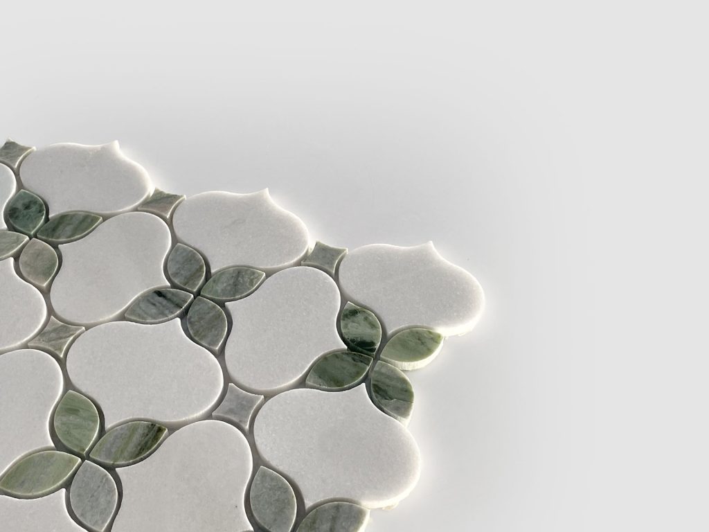 A close-up of decorative tilework with a floral pattern, featuring white and green petal-shaped tiles on a light gray background, extending from the left side and partially into the center.