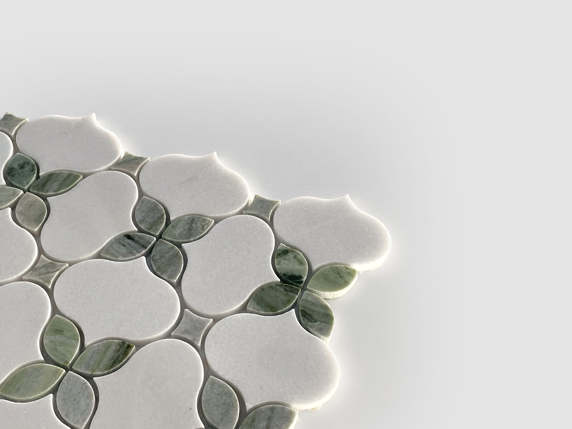 A close-up of decorative tilework with a floral pattern, featuring white and green petal-shaped tiles on a light gray background, extending from the left side and partially into the center.