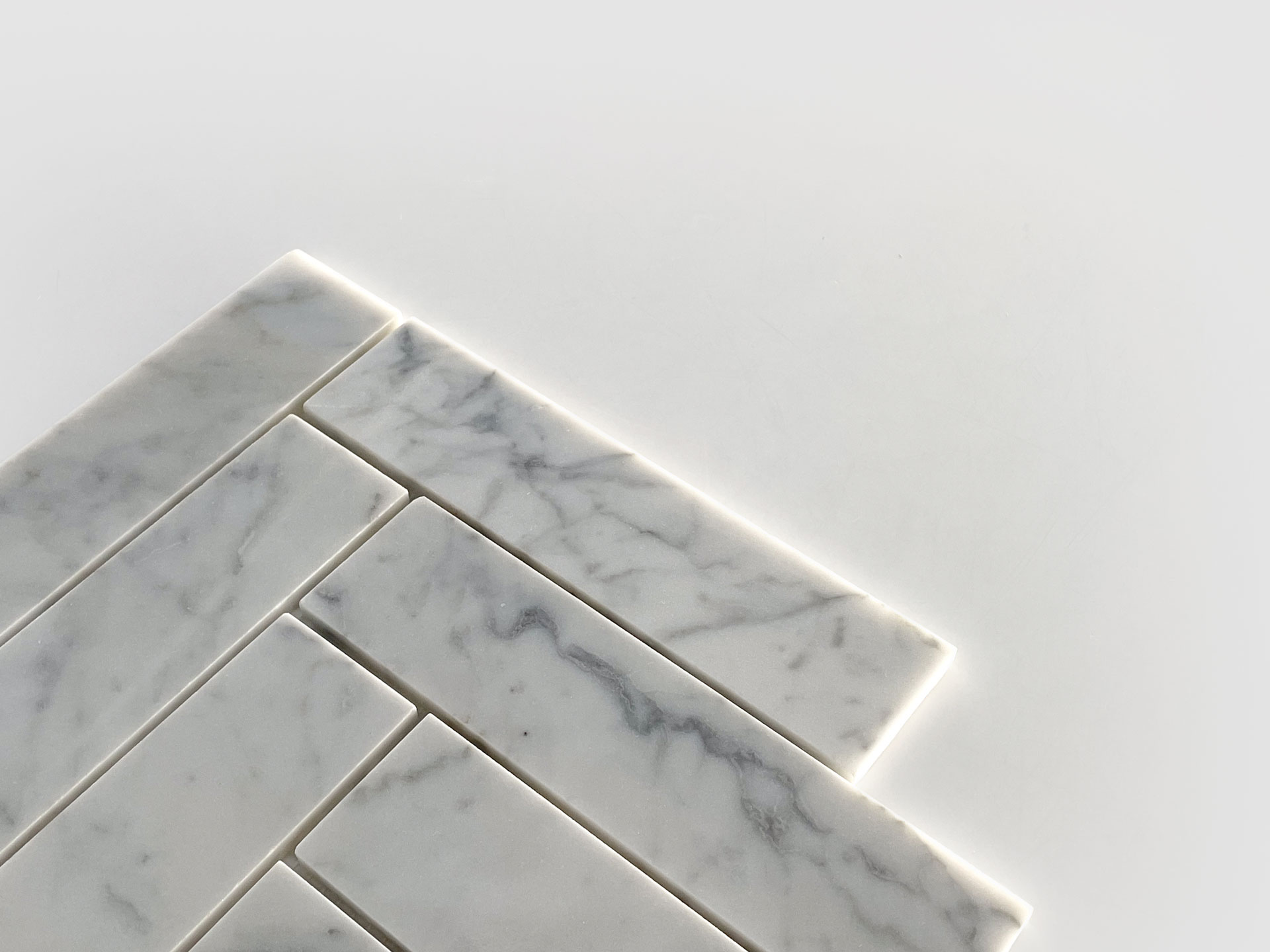 Several rectangular white marble tiles with subtle gray veining are arranged in a staggered pattern on a white surface, with bright lighting accentuating the edges of the tiles.