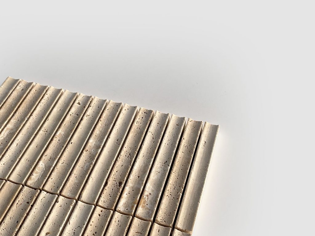 A close-up of beige, rectangular tiles with grooved and slightly porous surfaces, arranged in neat rows on a white background. The image is minimalistic with ample negative space.