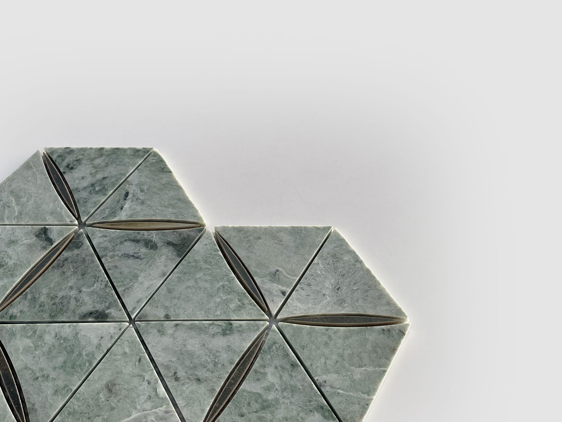 Geometric tile pattern with greenish-gray triangular tiles, arranged in a hexagonal formation on a white background. Some tiles have a thin, dark oval in the center. The design is partially shown, with tiles on the left side.