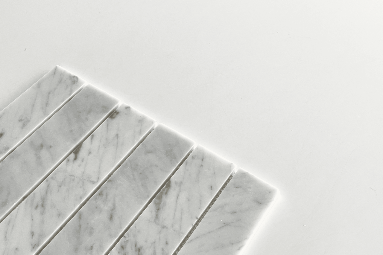 Seven rectangular strips of white marble with gray veining are arranged in parallel on a white surface, occupying the lower left corner of the image with ample negative space around them.