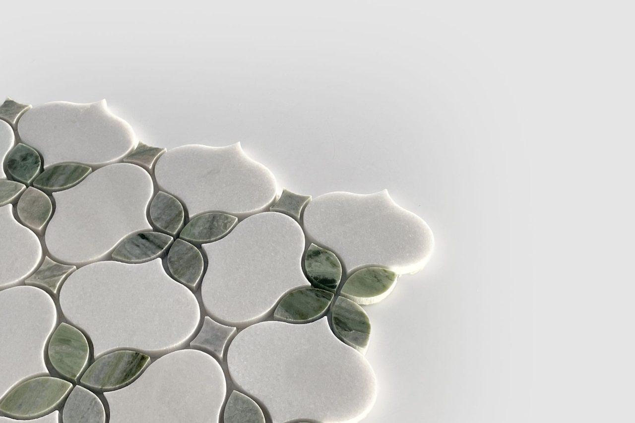 A close-up of decorative tilework with a floral pattern, featuring white and green petal-shaped tiles on a light gray background, extending from the left side and partially into the center.