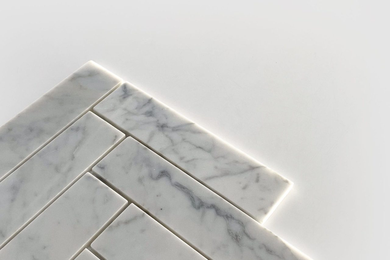 Several rectangular white marble tiles with subtle gray veining are arranged in a staggered pattern on a white surface, with bright lighting accentuating the edges of the tiles.