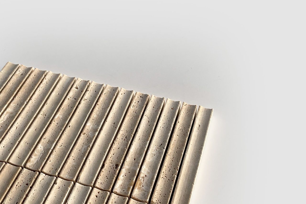 A close-up of beige, rectangular tiles with grooved and slightly porous surfaces, arranged in neat rows on a white background. The image is minimalistic with ample negative space.