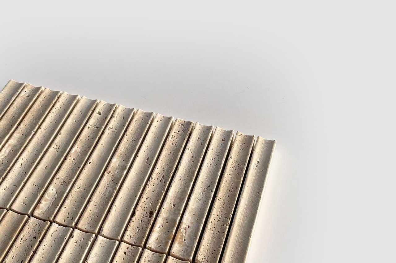 A close-up of beige, rectangular tiles with grooved and slightly porous surfaces, arranged in neat rows on a white background. The image is minimalistic with ample negative space.