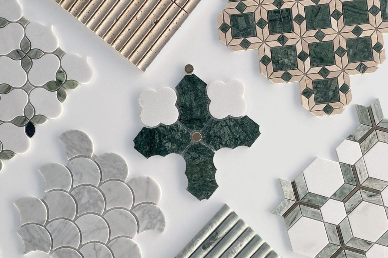 An arrangement of patterned tiles in various shapes, colors, and textures, including green, white, and beige tones, displayed on a white surface. The tiles feature geometric, scalloped, and floral designs.